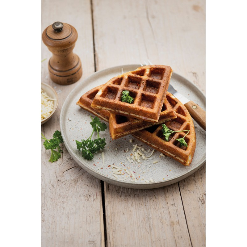 Wafels op een bord, peterselie, kaas en pepermolen op een houten tafel.