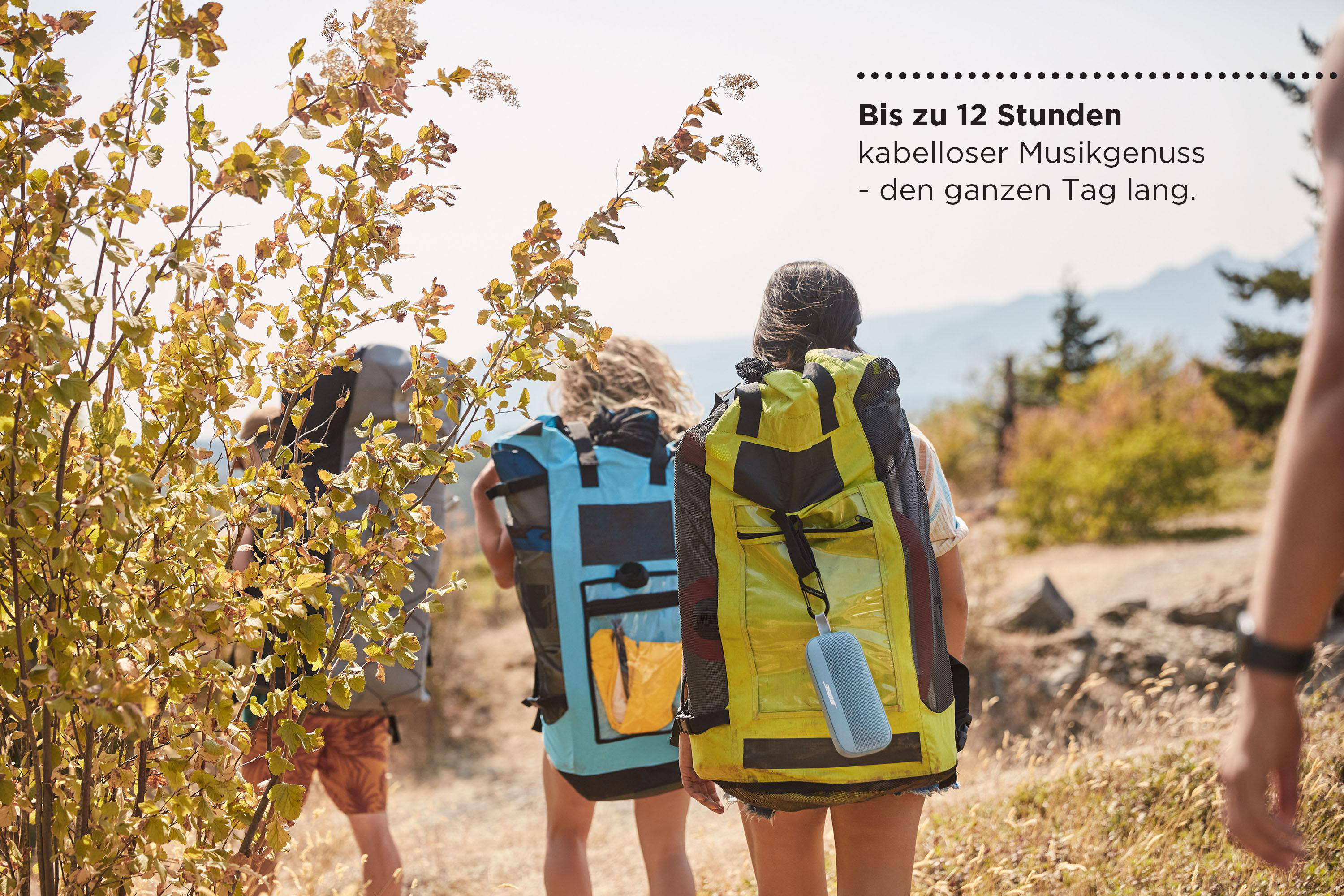 Wanderer in sonniger Umgebung mit Rucksäcken und einem kleinen, grauen Lautsprecher.