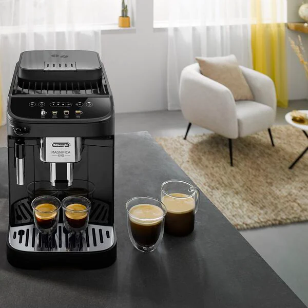 A black espresso machine with two glasses of espresso and a white chair in the background.