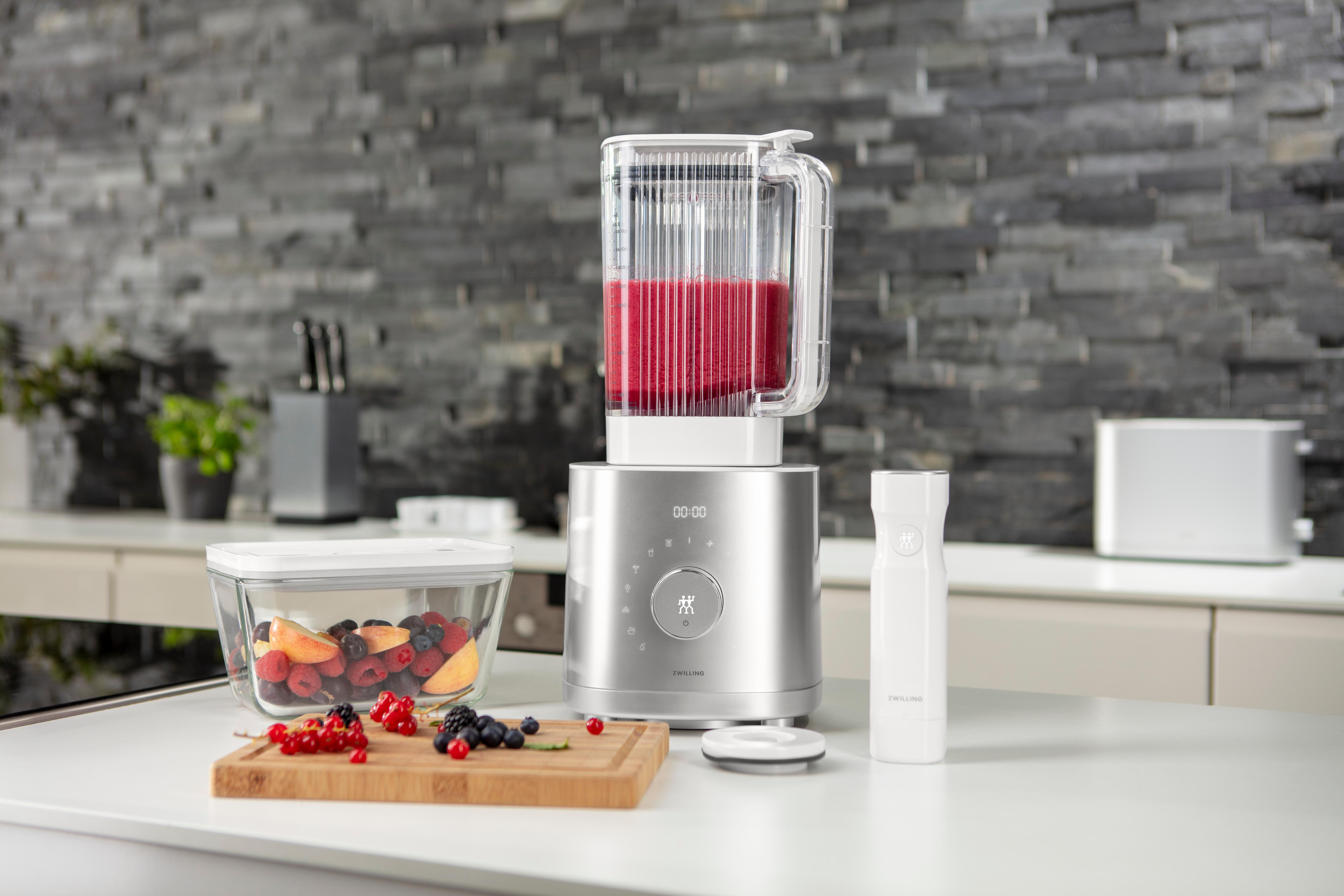 Ein Mixer mit roter Flüssigkeit und Früchten auf einem Tisch.