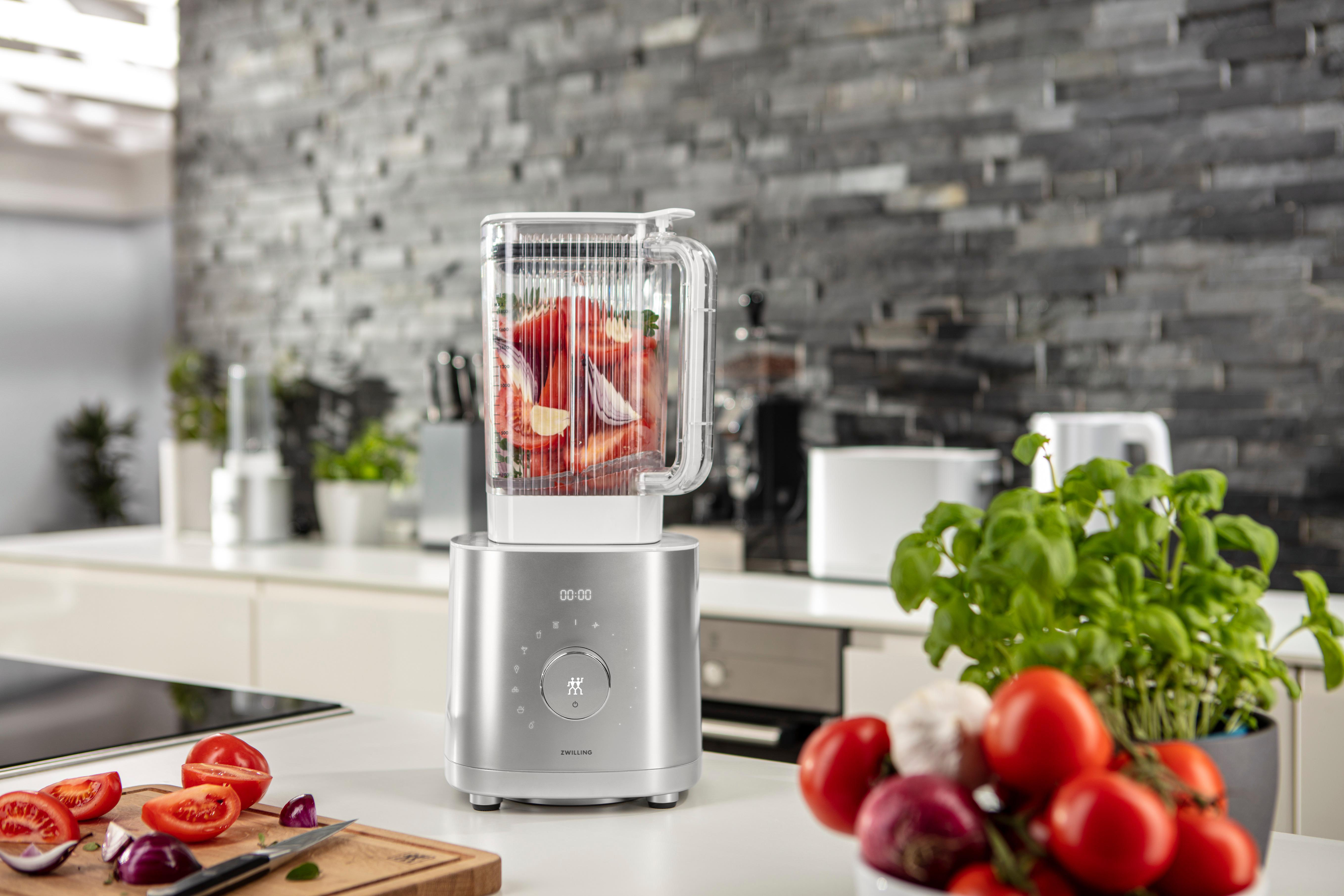 Edelstahl-Mixer mit Erdbeeren und Zwiebeln, Tomaten und Basilikumpflanze.