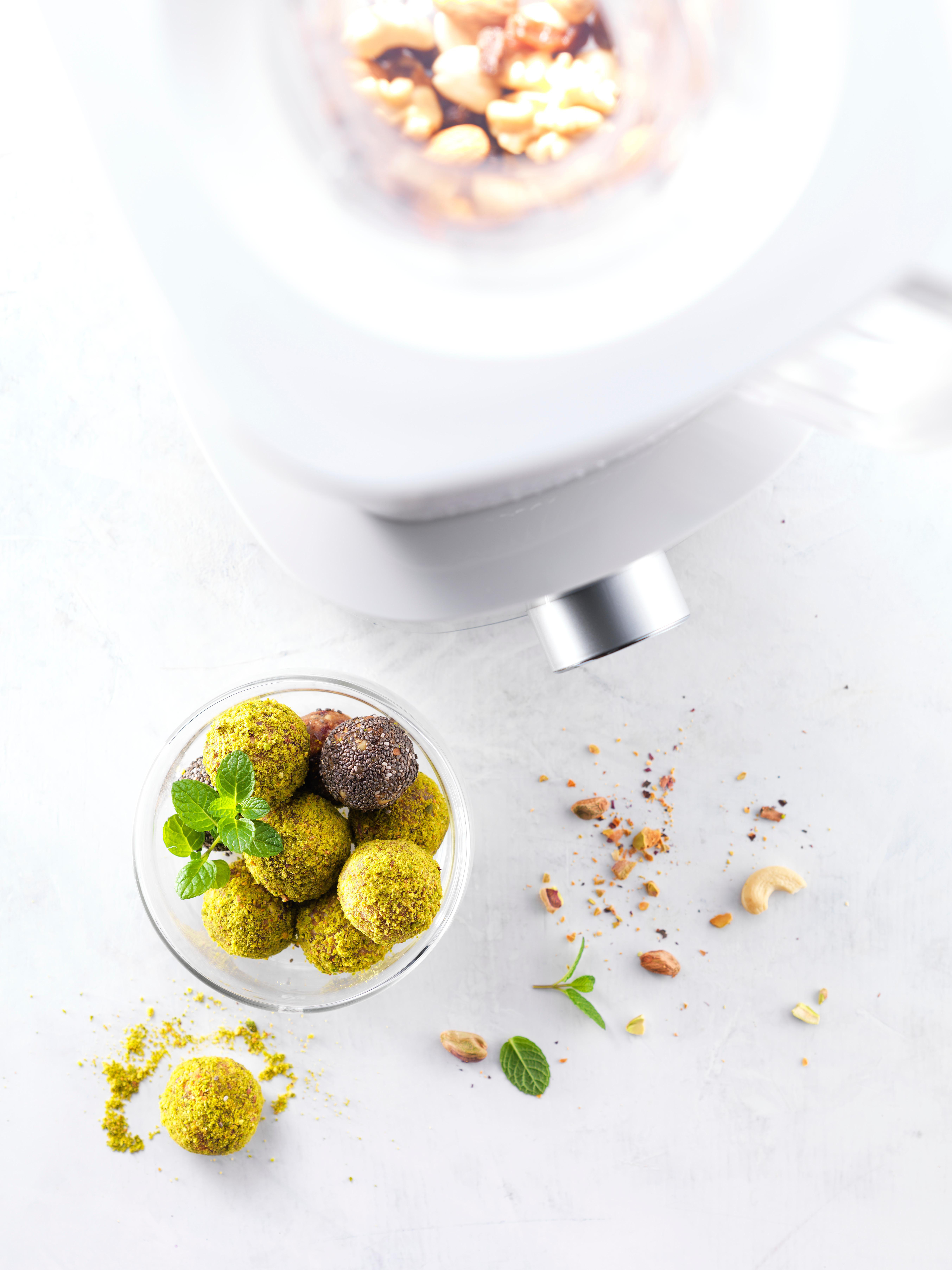 Draufsicht auf eine Schüssel mit grünen Kugeln, Nüssen und einem Mixer.