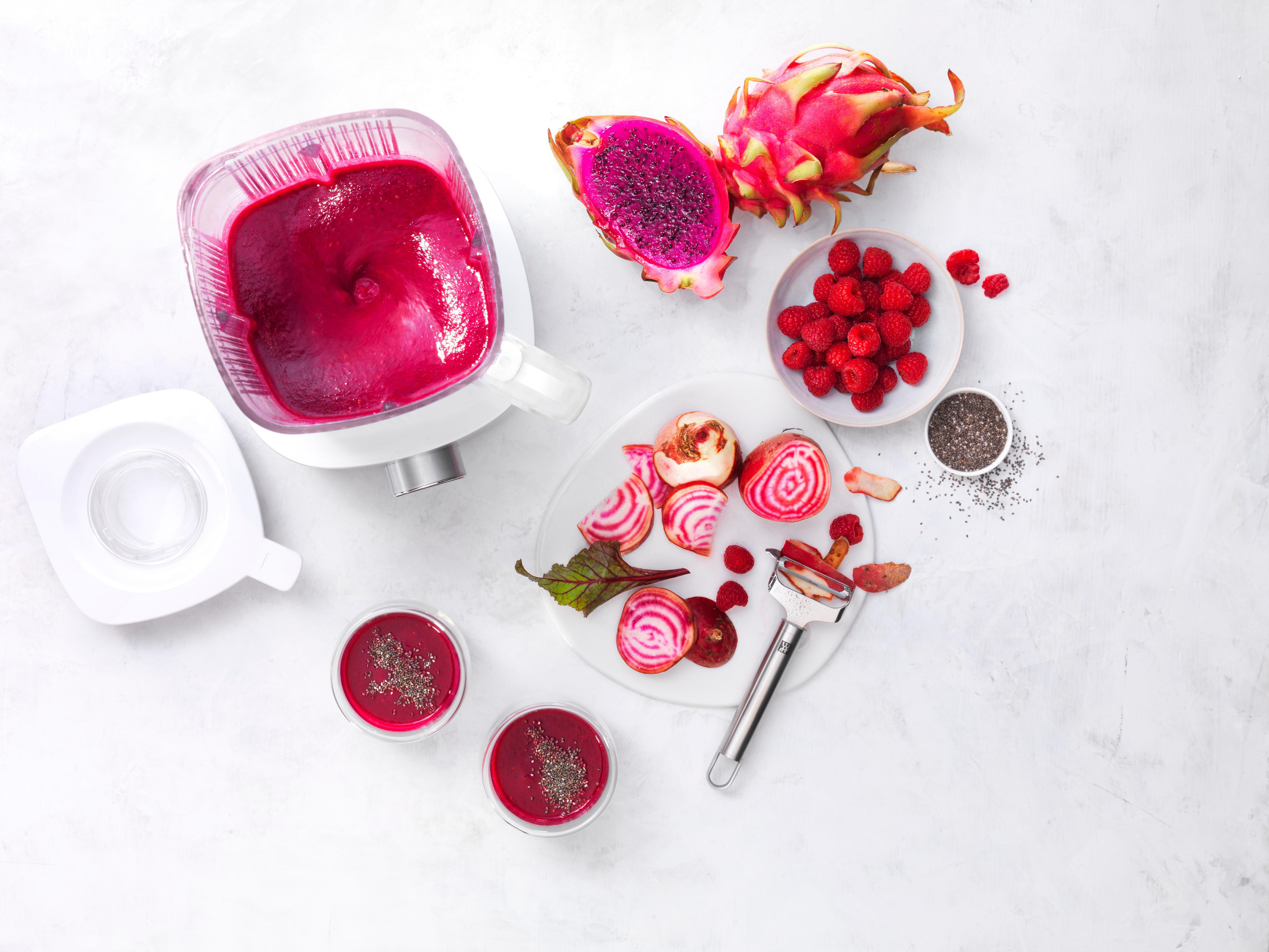Ein Mixer mit lila Smoothie. Drachenfrucht, Himbeeren und Rüben sind darum angeordnet.