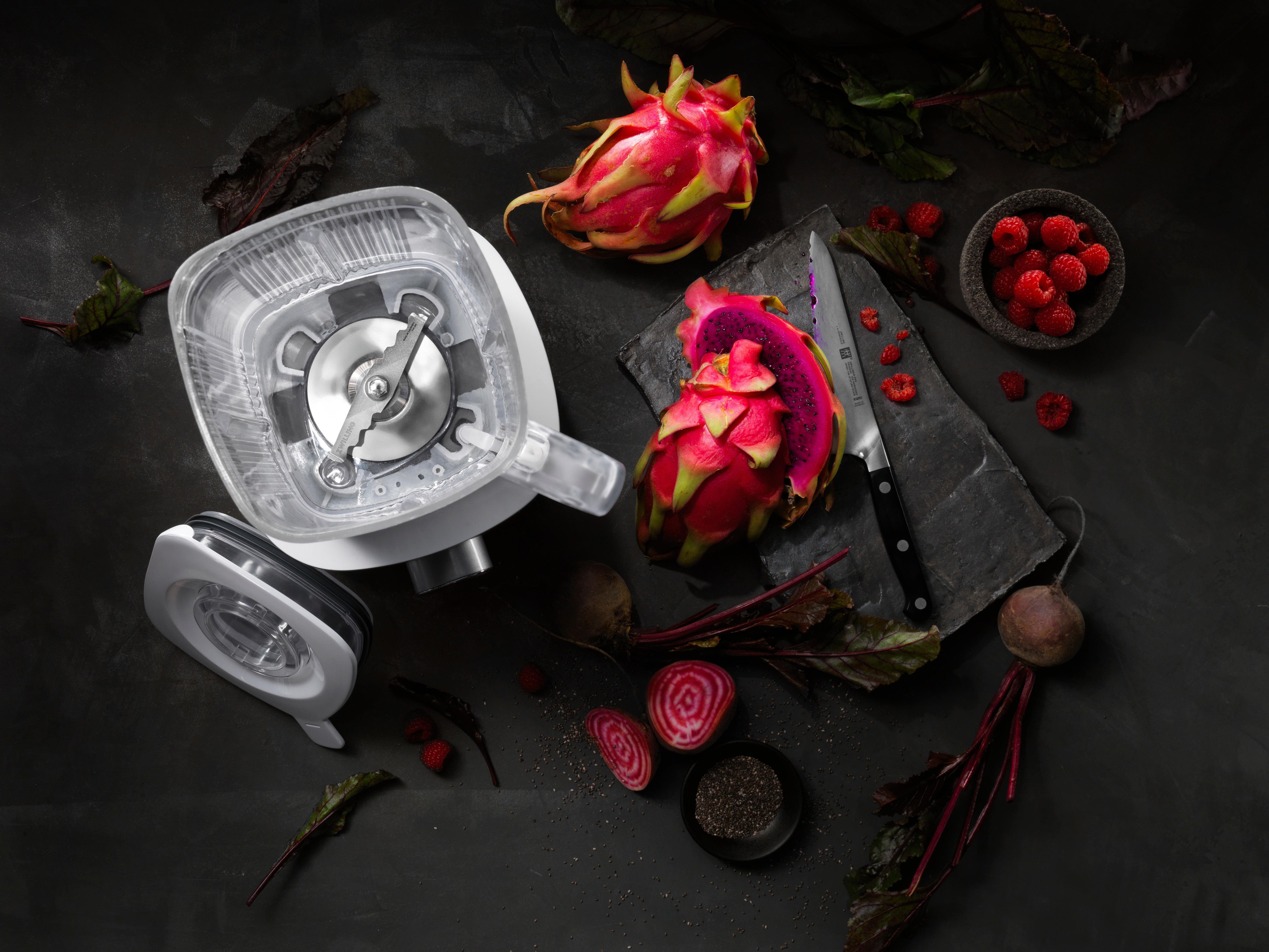 Mixer mit Drachenfrucht, Himbeeren, Rote Bete und einem Messer auf dunkler Oberfläche.