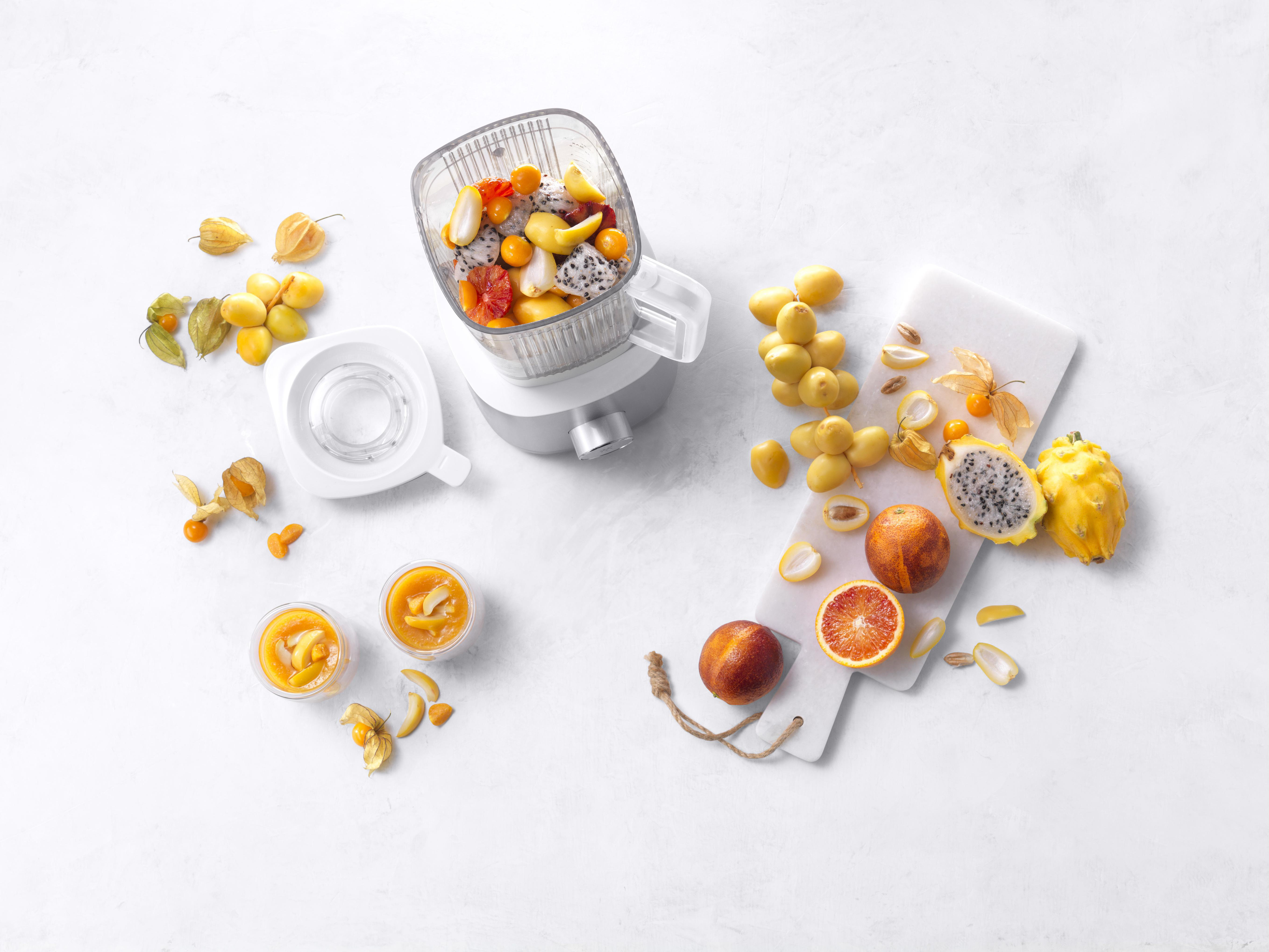 Mixer mit Früchten. Drachenfrüchte, Orangen und Physalis sind auf weißer Oberfläche angeordnet.