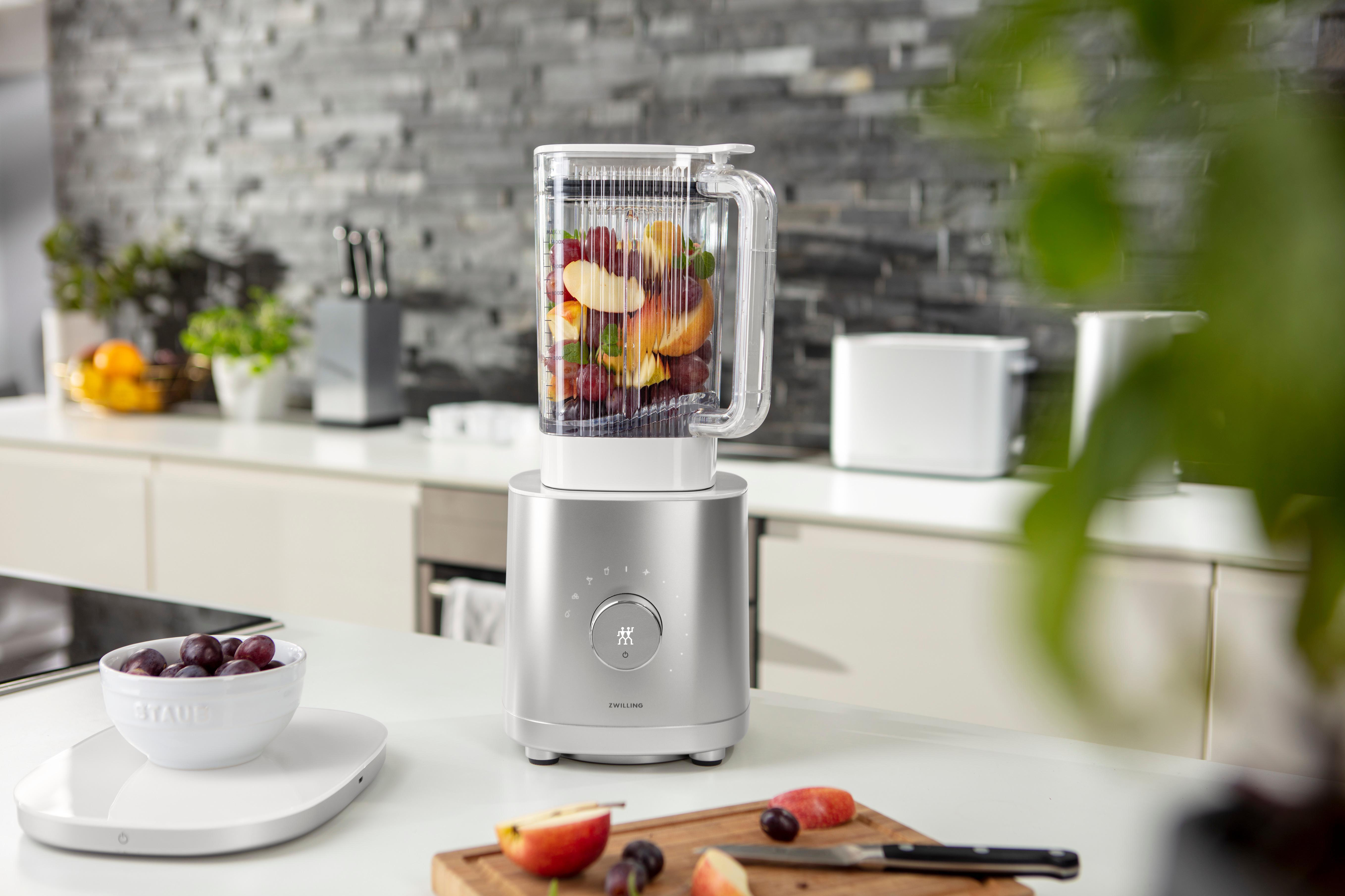 Ein silberner Mixer mit Früchten, auf einer Küchentheke mit anderen Gegenständen.