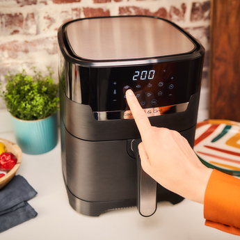 Person's hand pressing a button on a black air fryer with a digital display.