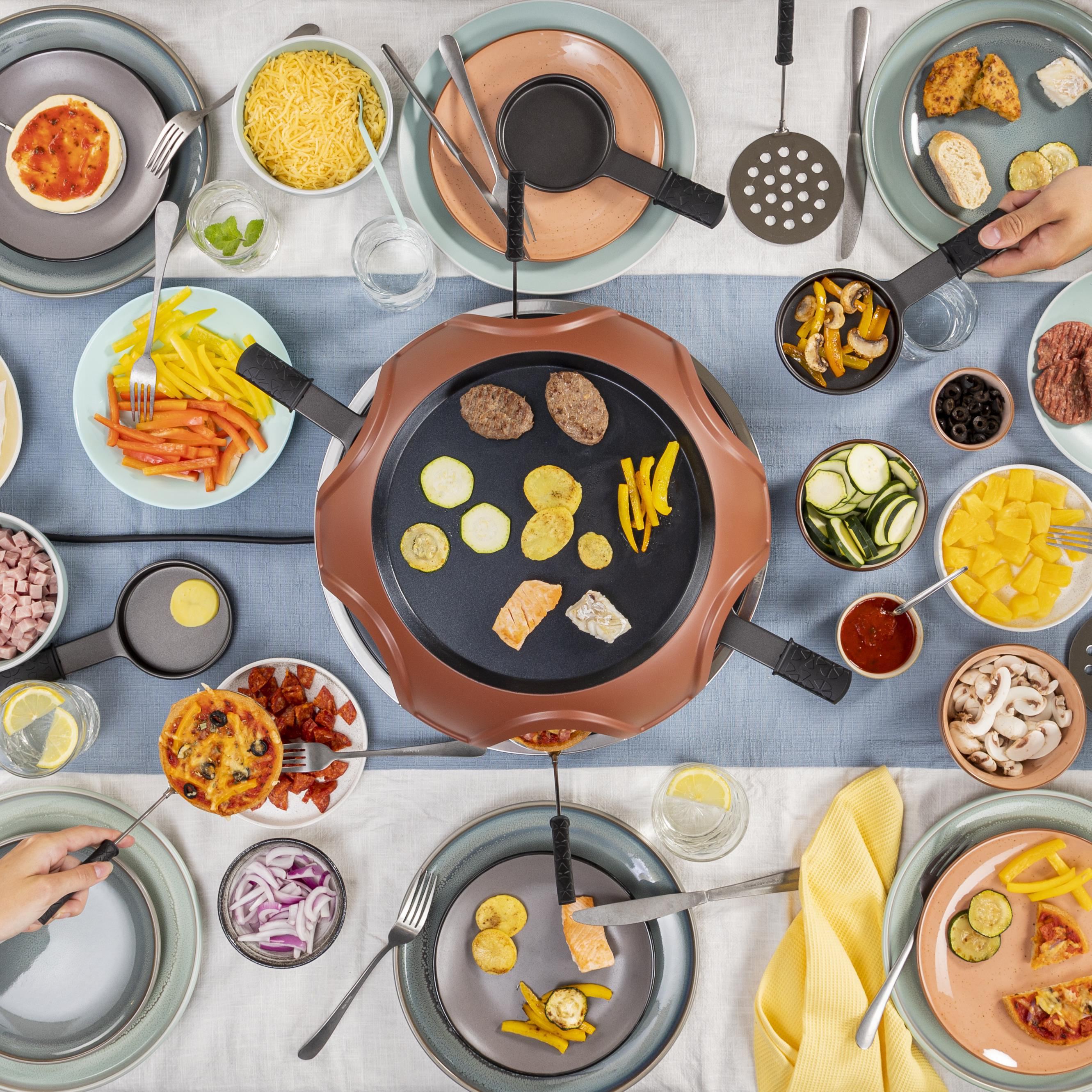 Draufsicht auf einen Tisch, der für Raclette gedeckt ist. Verschiedene Zutaten, Utensilien und Teller.
