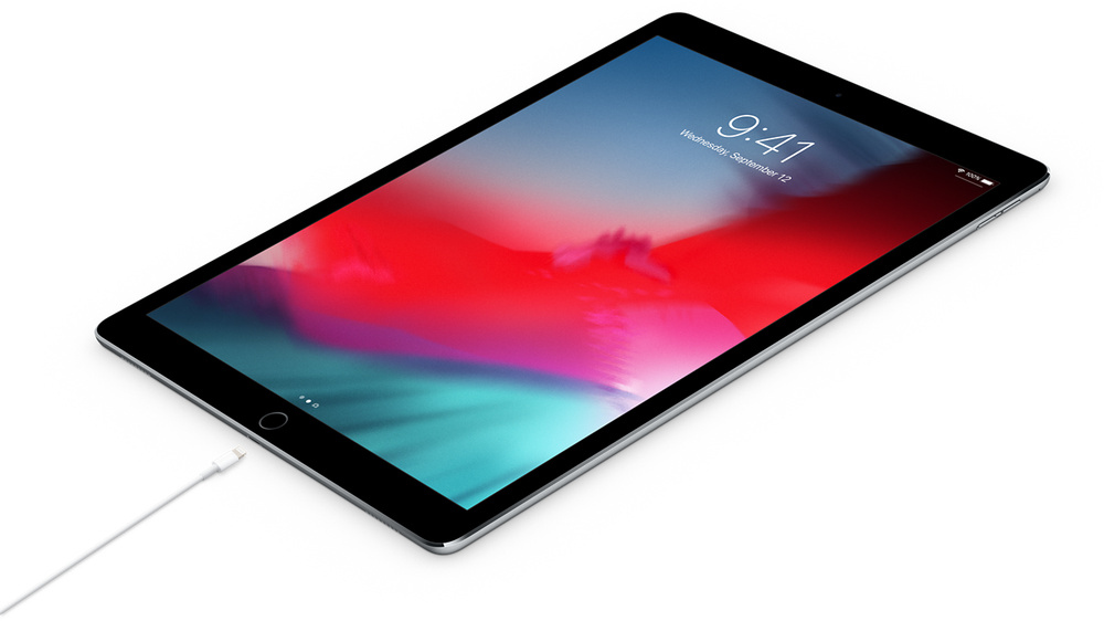 An iPad Pro with a black frame and a white charging cable on a white background.