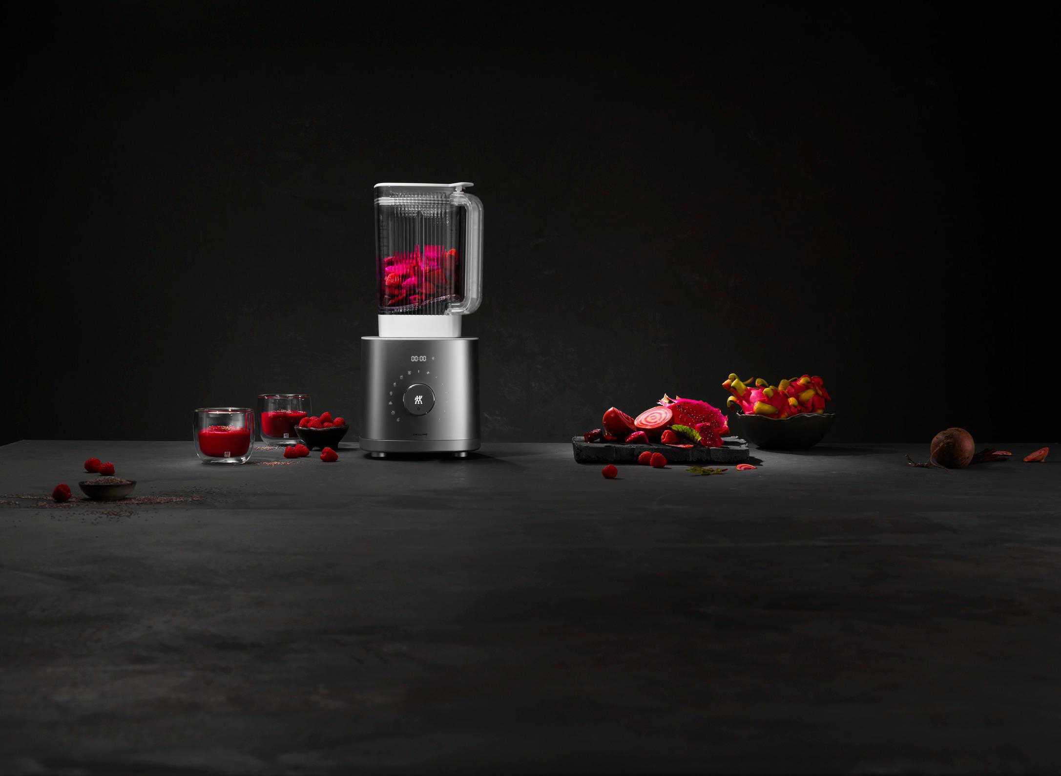 Ein Mixer mit einem Glas voller roter Früchte. Weitere Früchte sind drumherum.