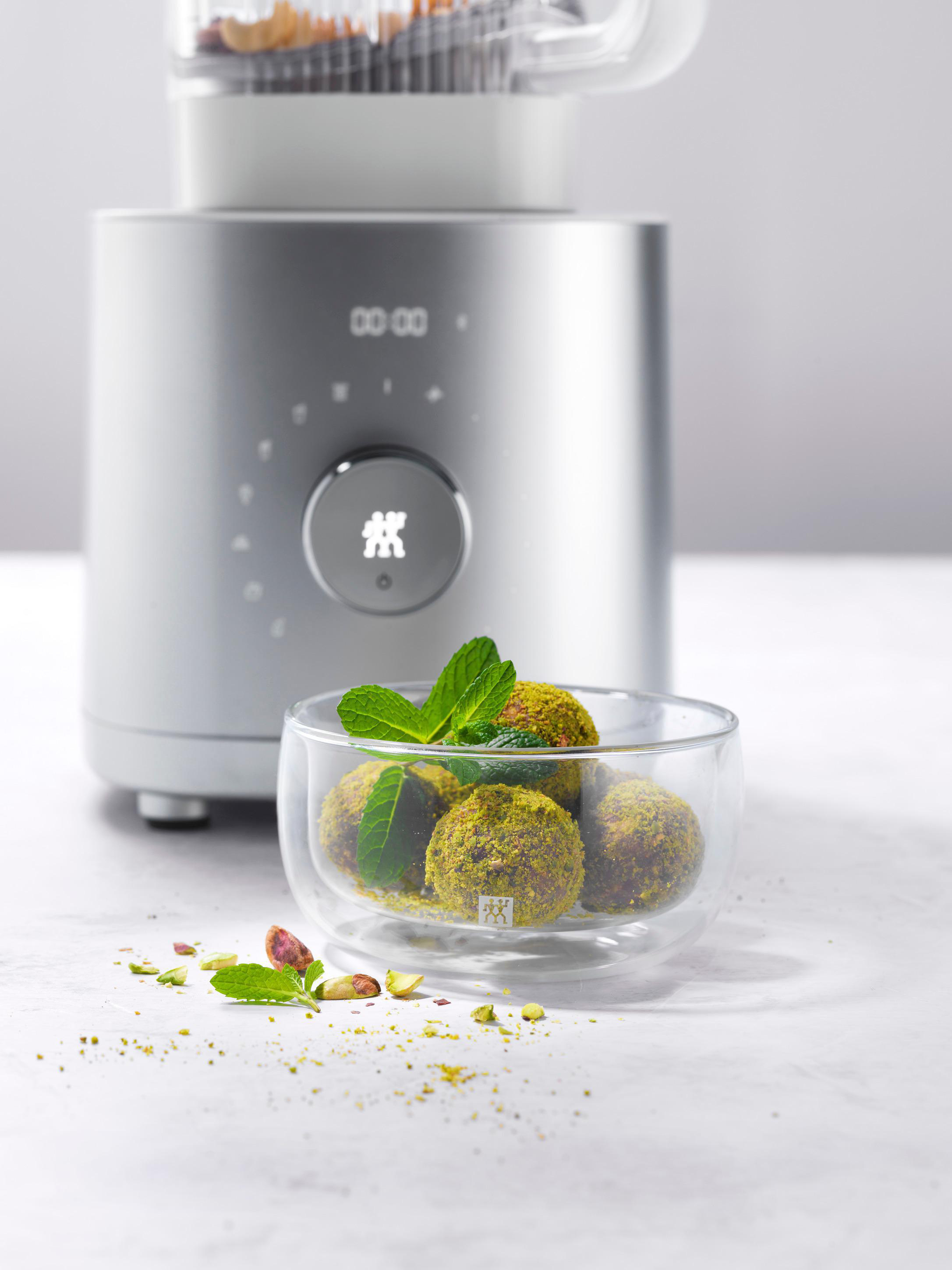 Silberner Mixer mit einer Schüssel mit pistaziengedeckten Kugeln und Minzzweigen.