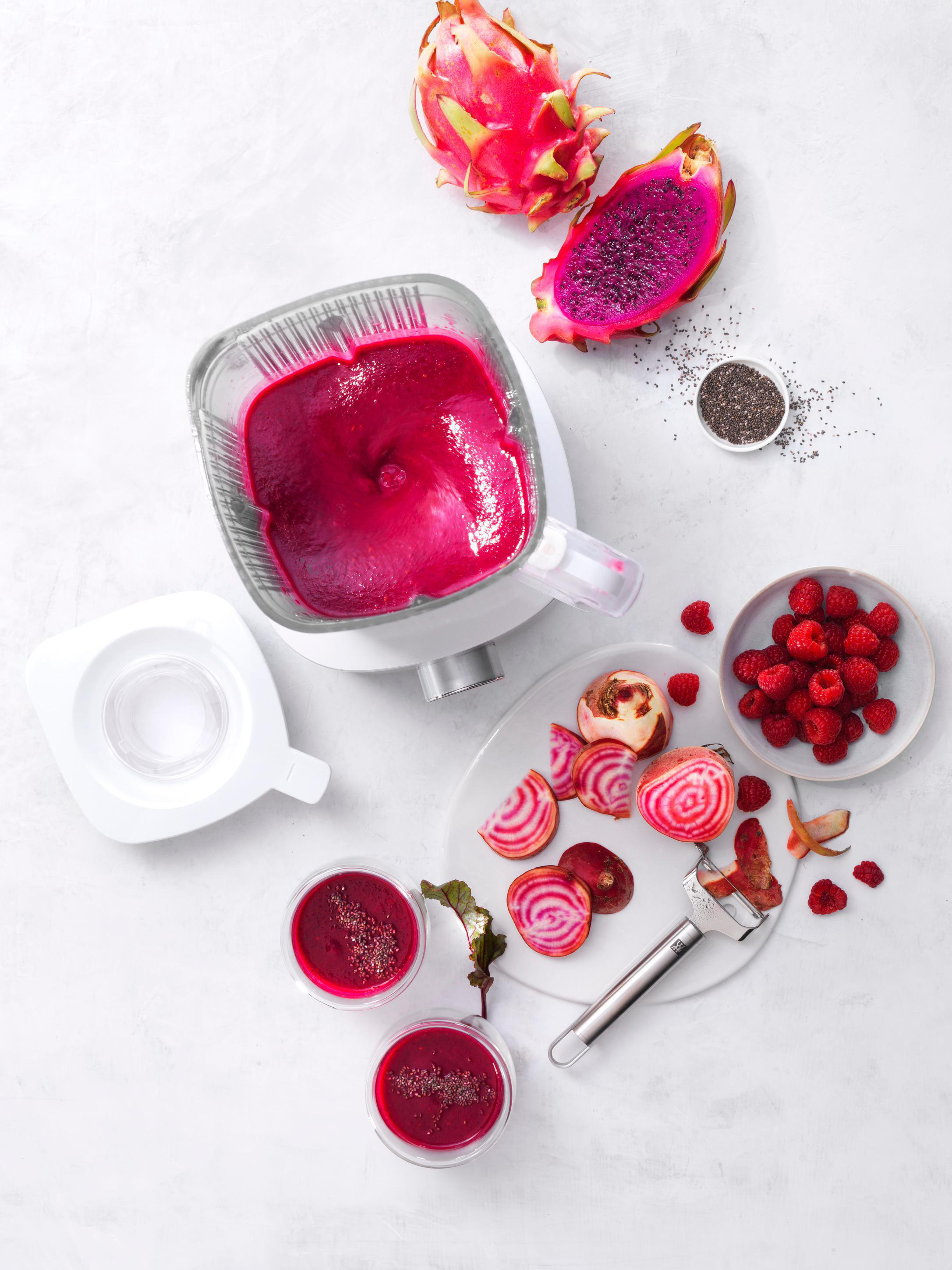 Eine Draufsicht auf Lebensmittelzutaten. Ein Mixer mit pinkfarbenem Smoothie, Drachenfrucht und Rüben.