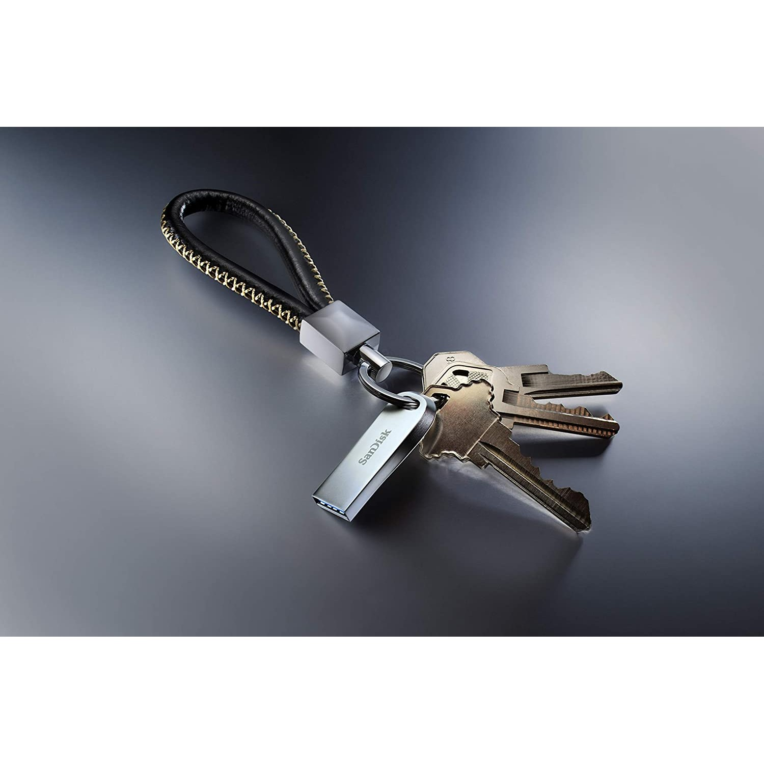 Una unidad USB plateada unida a llaves con un cordón negro y dorado.