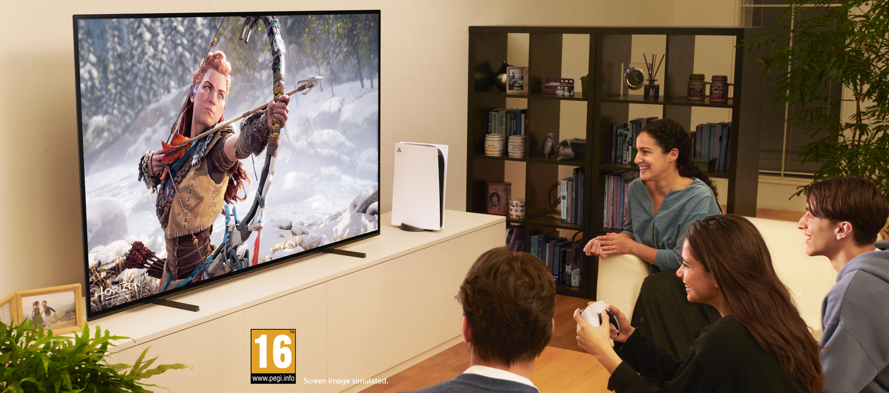 Leute schauen ein Spiel am Fernseher. Eine Konsole steht auf dem Tisch. Leute sitzen und halten Gamecontroller.