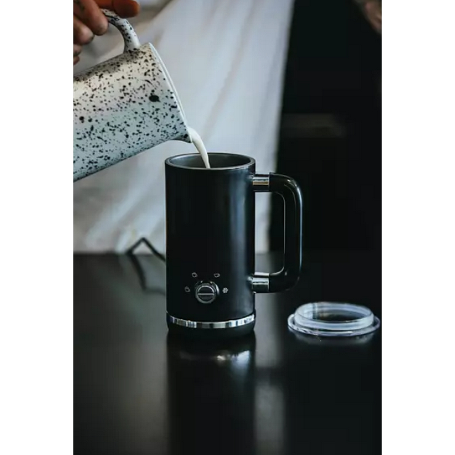 Una persona vierte leche de una jarra moteada en una taza de café negra.