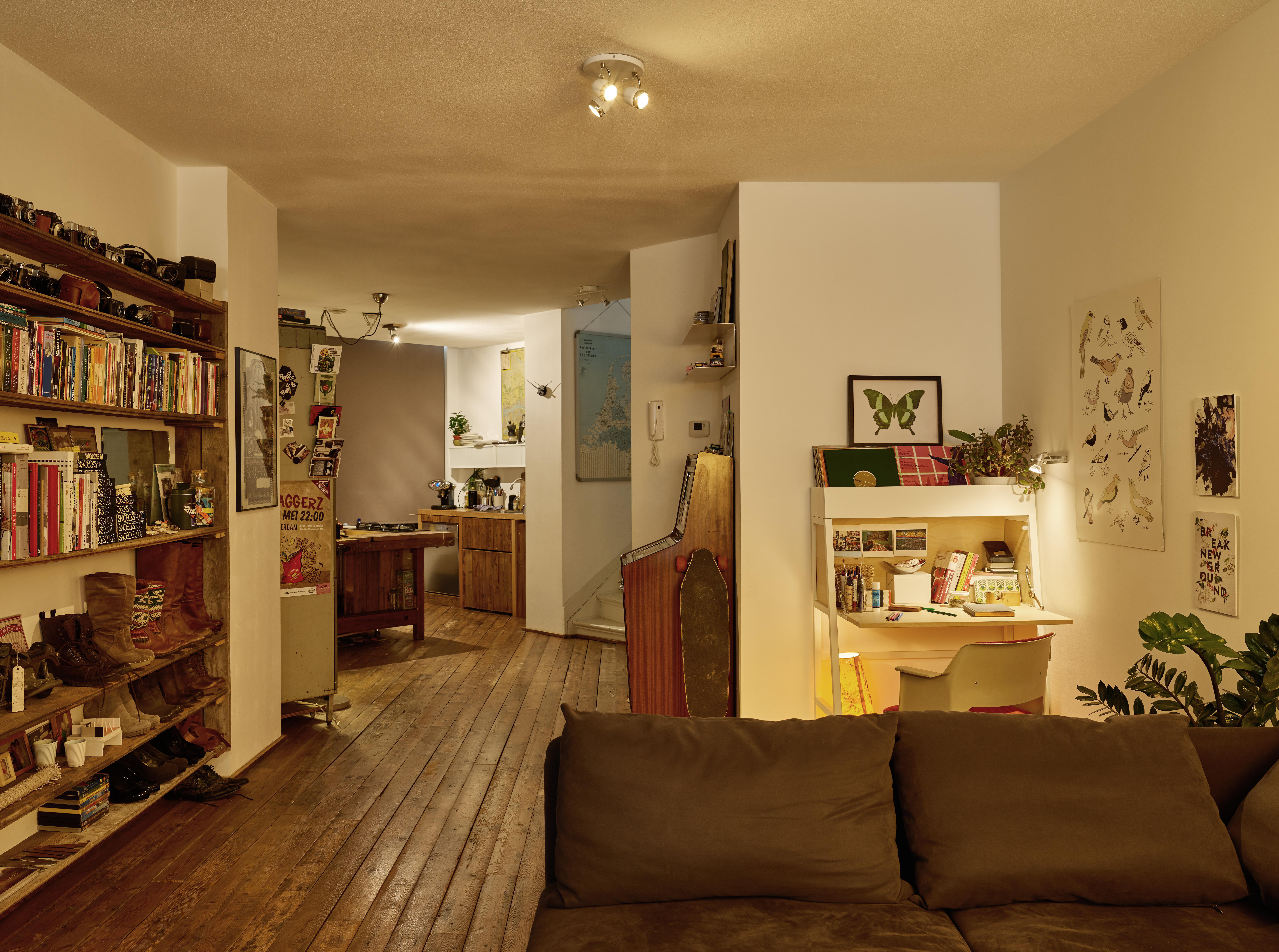 Innenaufnahme eines Wohnzimmers mit Holzböden. Bücherregale, Schreibtisch und Sofa sind sichtbar.