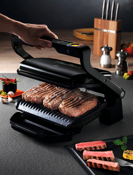Une personne grillant des steaks sur un grill noir, avec des steaks cuits sur le côté.