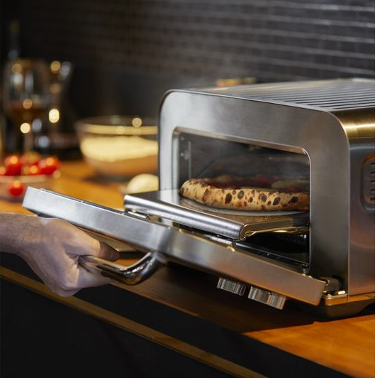 Egy személy kinyit egy ezüst pizza sütőt, egy sült pizzát mutatva benne egy tálcán.