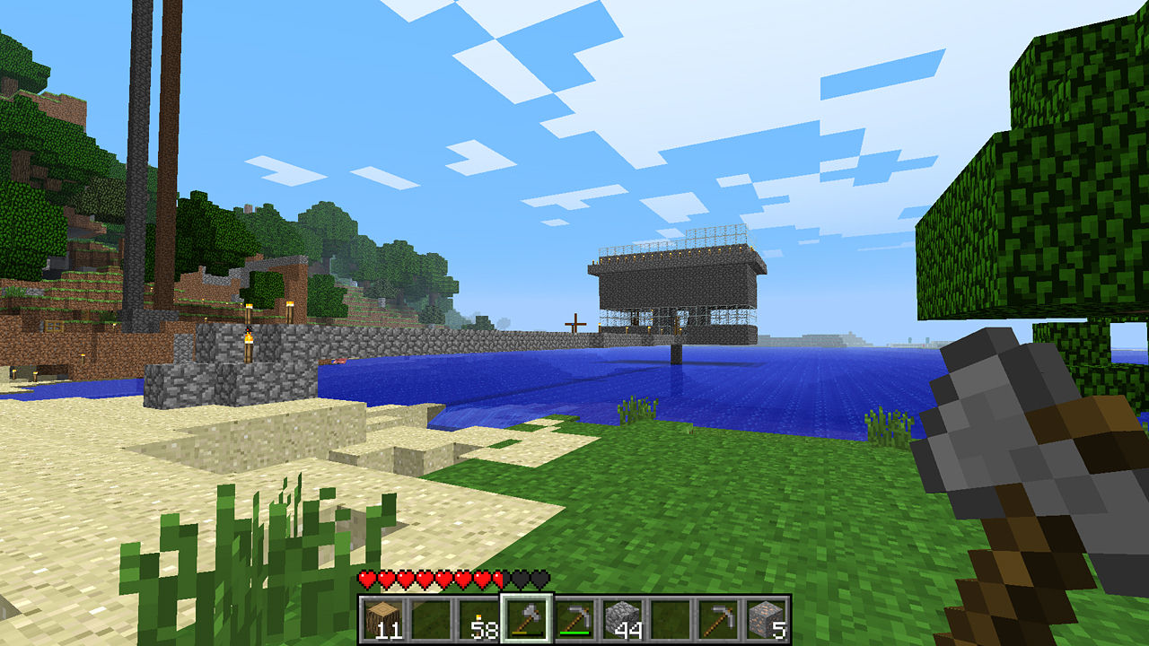 Visuale di gioco di Minecraft, giocatore che tiene un piccone, con una casa sull'acqua.