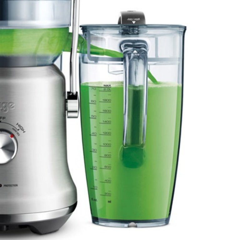 A juicer with green juice in a clear container, measuring liquid volume.