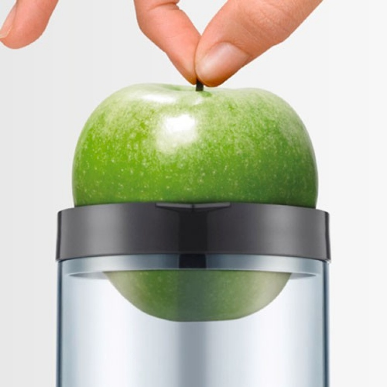 A green apple sits in a clear container. A hand is placing the apple down.