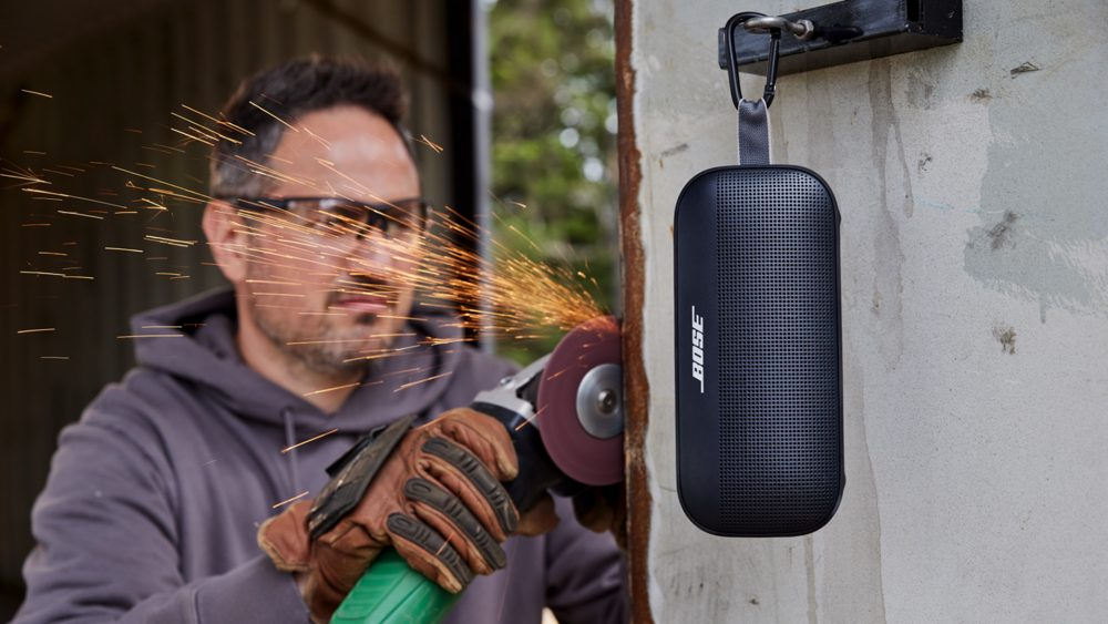 Man gebruikt slijpmachine met vonken nabij zwarte Bose speaker aan grijze muur.