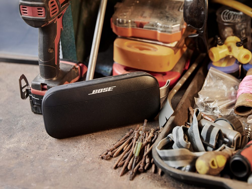 Un haut-parleur BOSE noir sur une surface en béton parmi des outils et autres objets.