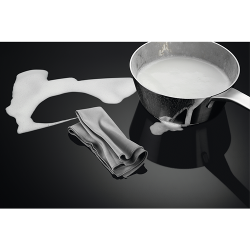 A pan with white foamy liquid spilled on a glossy black surface. A grey cloth on the left.