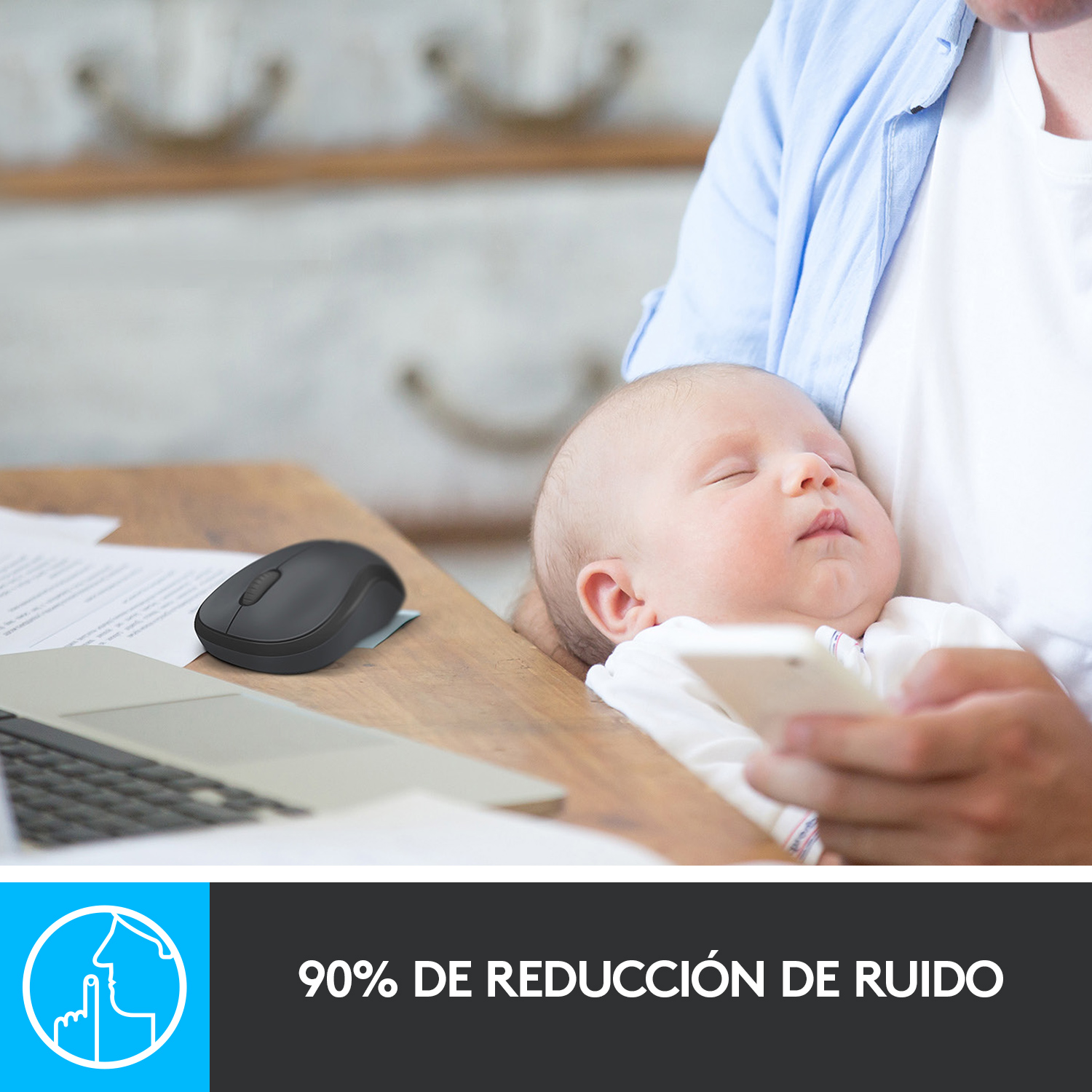 Un bebé dormido sostenido por un hombre. Un ratón y un portátil en un escritorio.