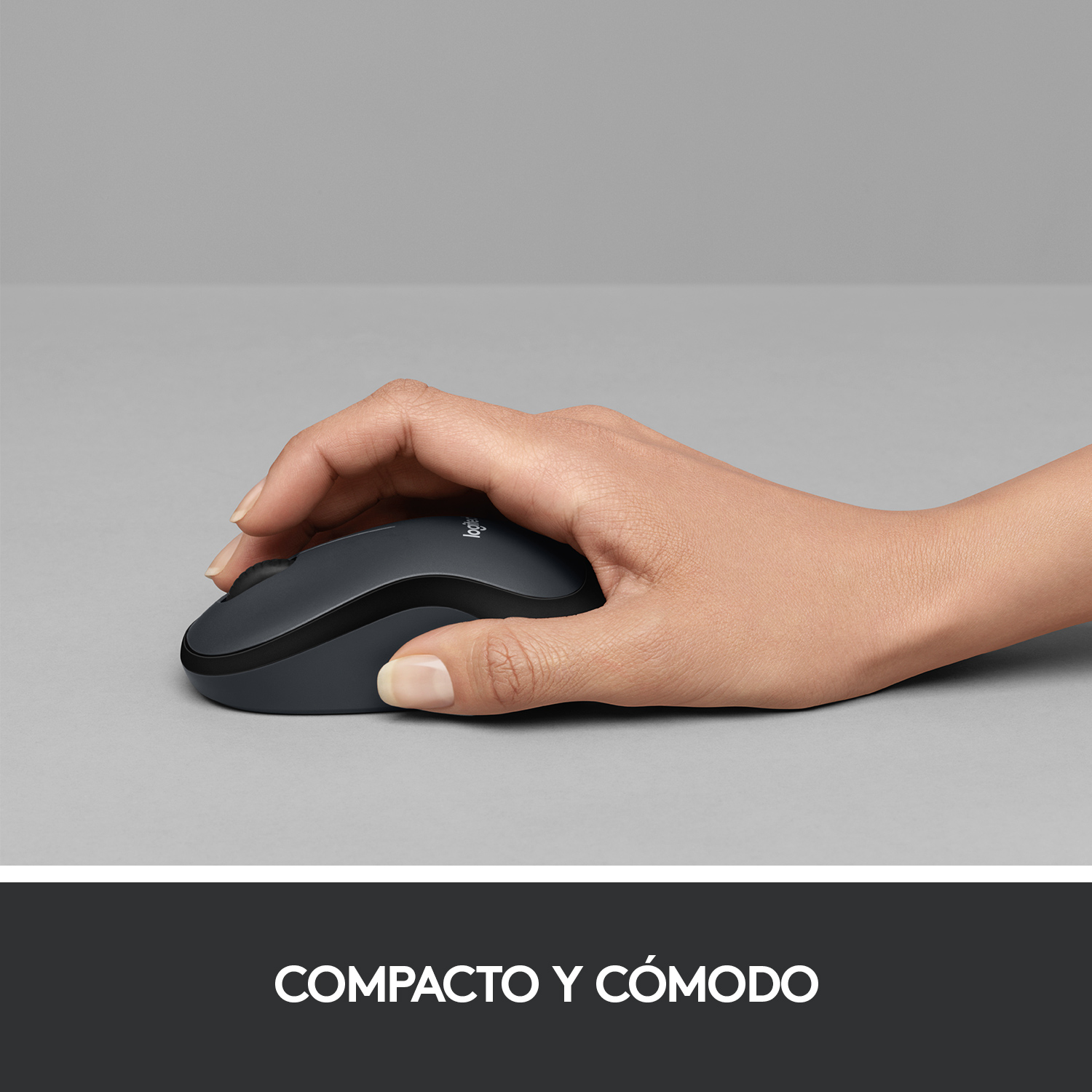 Mano sosteniendo un ratón Logitech gris oscuro sobre superficie gris claro.