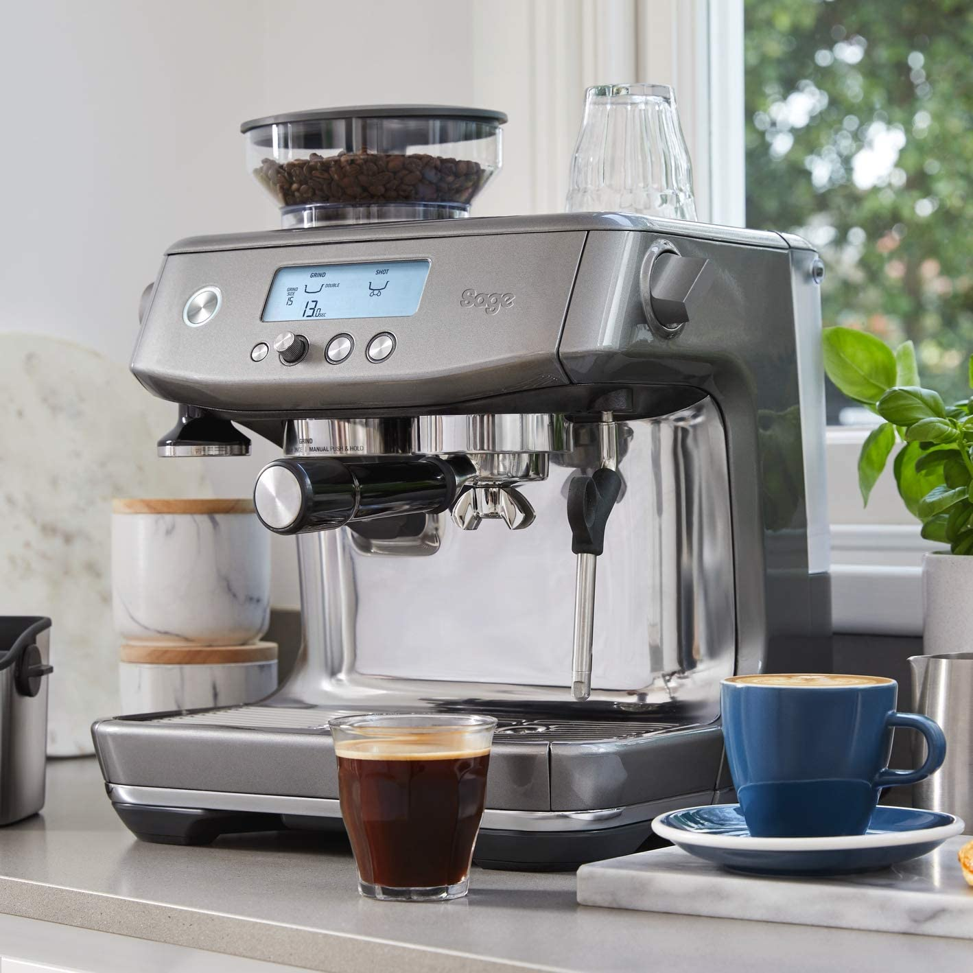 A grey espresso machine with a coffee cup and a glass of espresso.