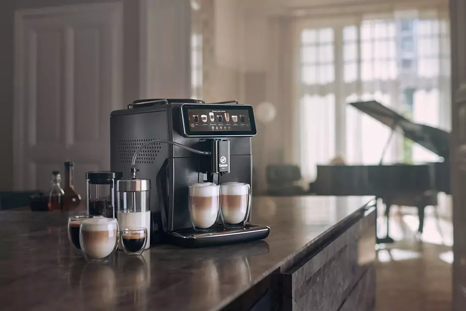 Macchina per caffè espresso nera con due tazze di latte in vetro. Bancone della cucina con altri accessori.