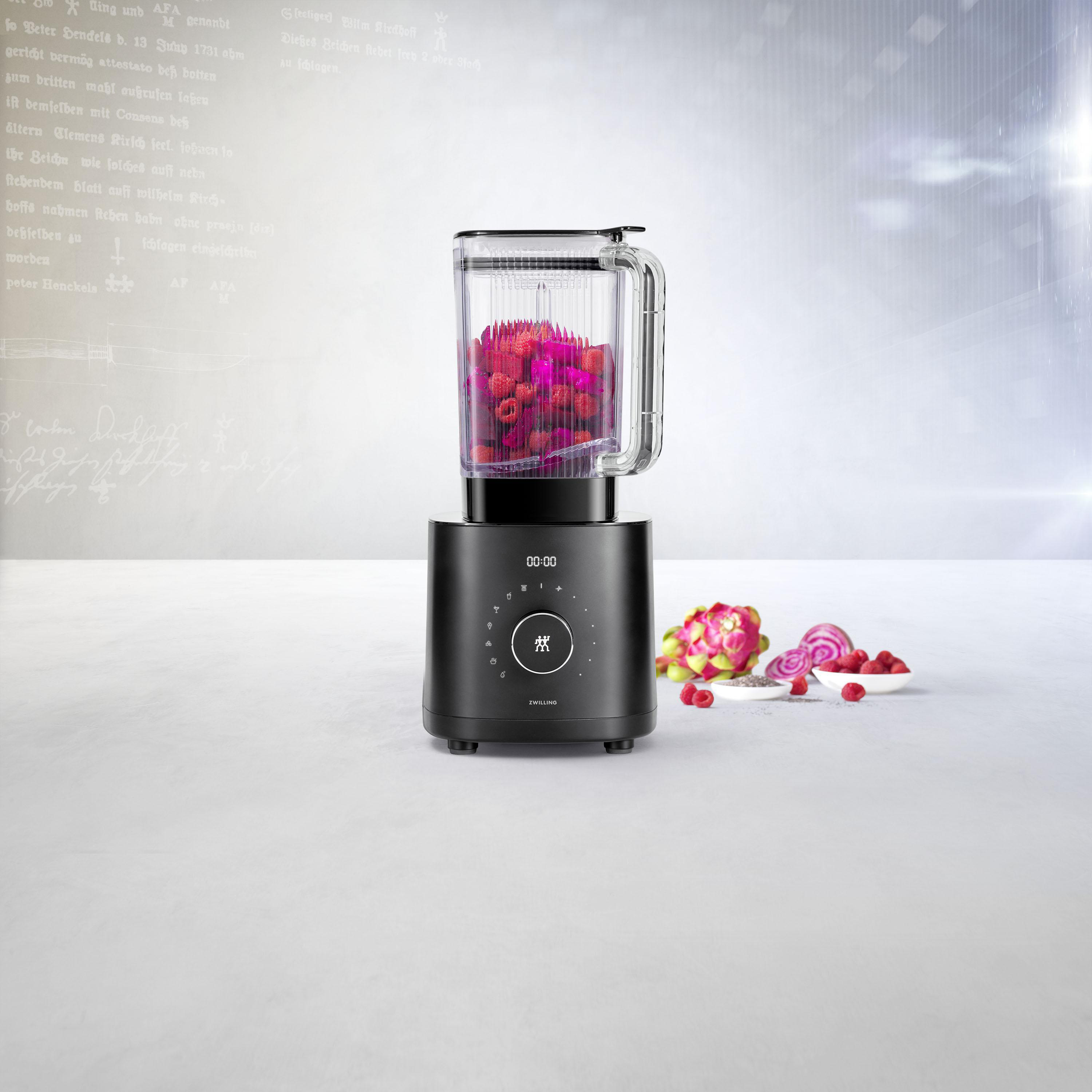 Ein schwarzer Mixer mit Himbeeren darin, eine Schüssel mit Himbeeren und ein paar geschnittene Rüben stehen auf dem Tisch.