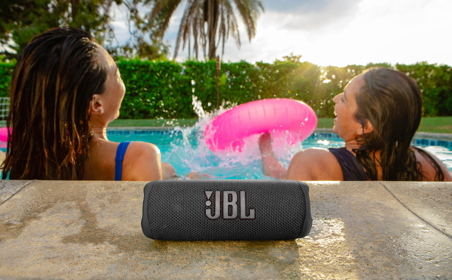 Deux femmes dans une piscine avec un haut-parleur JBL sur une surface en pierre. Une a une bouée rose.