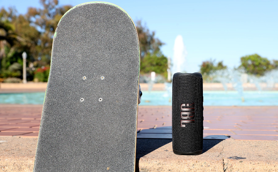 Enceinte JBL noire à côté d'un skateboard. Fontaine en arrière-plan par une journée ensoleillée.