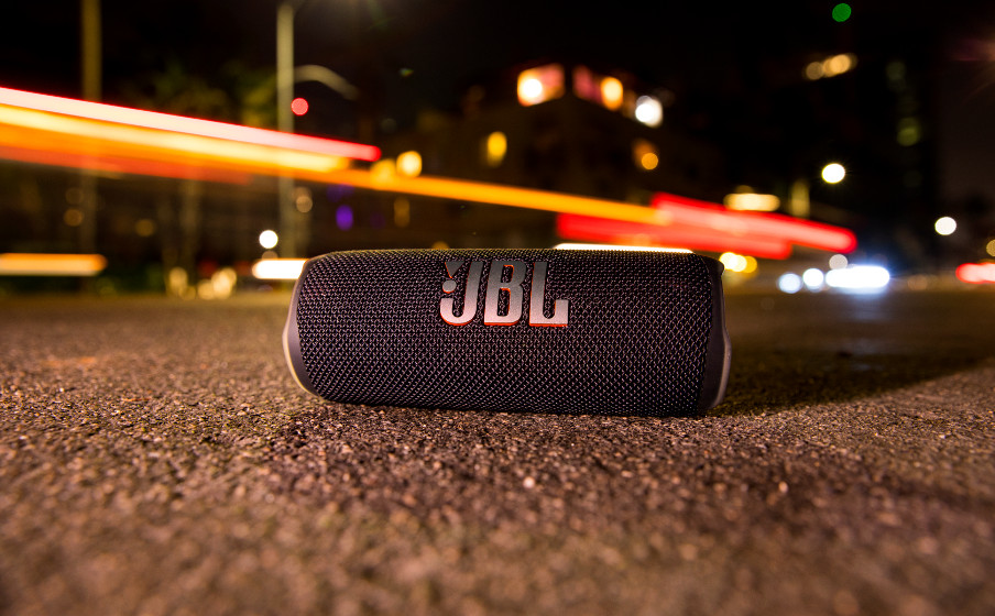 Un haut-parleur JBL noir sur la route la nuit, avec des feux de voiture flous en arrière-plan.