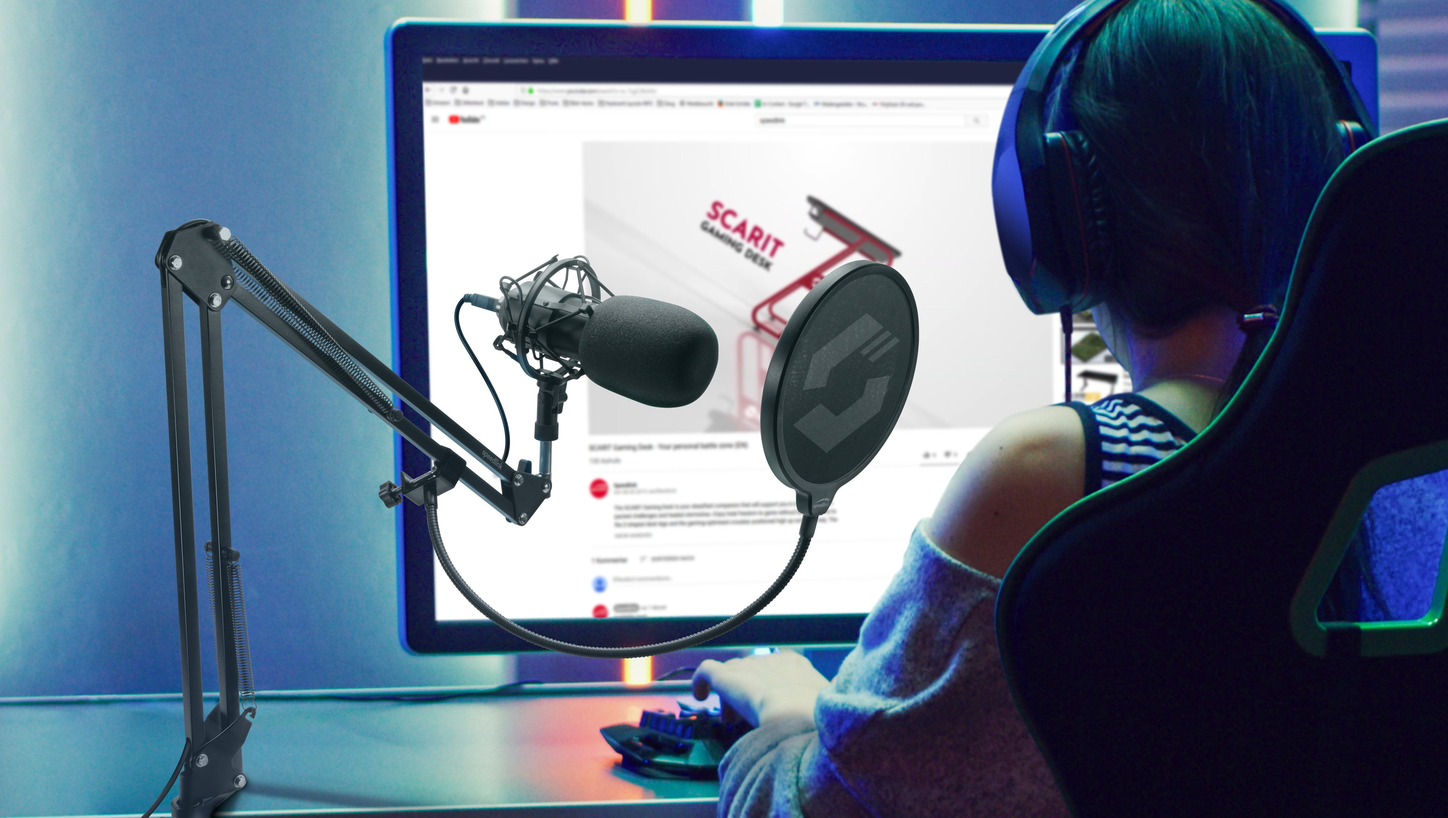 Eine Person in einem Gaming-Setup mit Mikrofon, Monitor, der einen Gaming-Schreibtisch zeigt, und Headset.