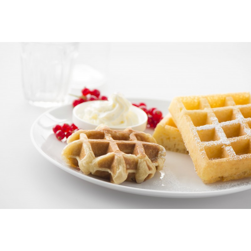 Waffles with whipped cream, red currants, and powdered sugar on a white plate.