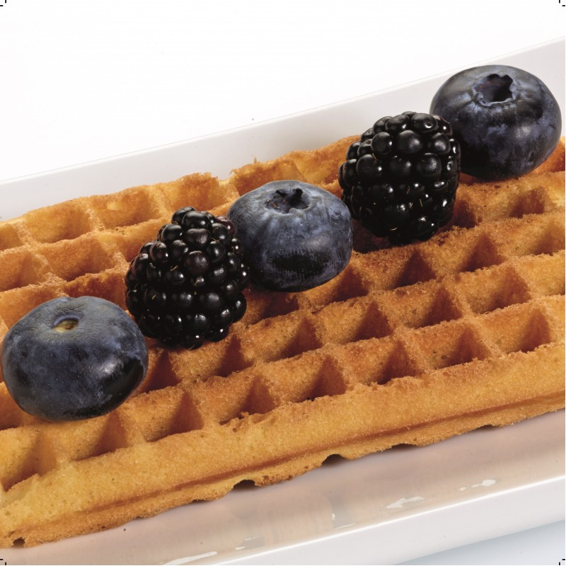 Waffle with blueberries and blackberries arranged in a row on a white plate.