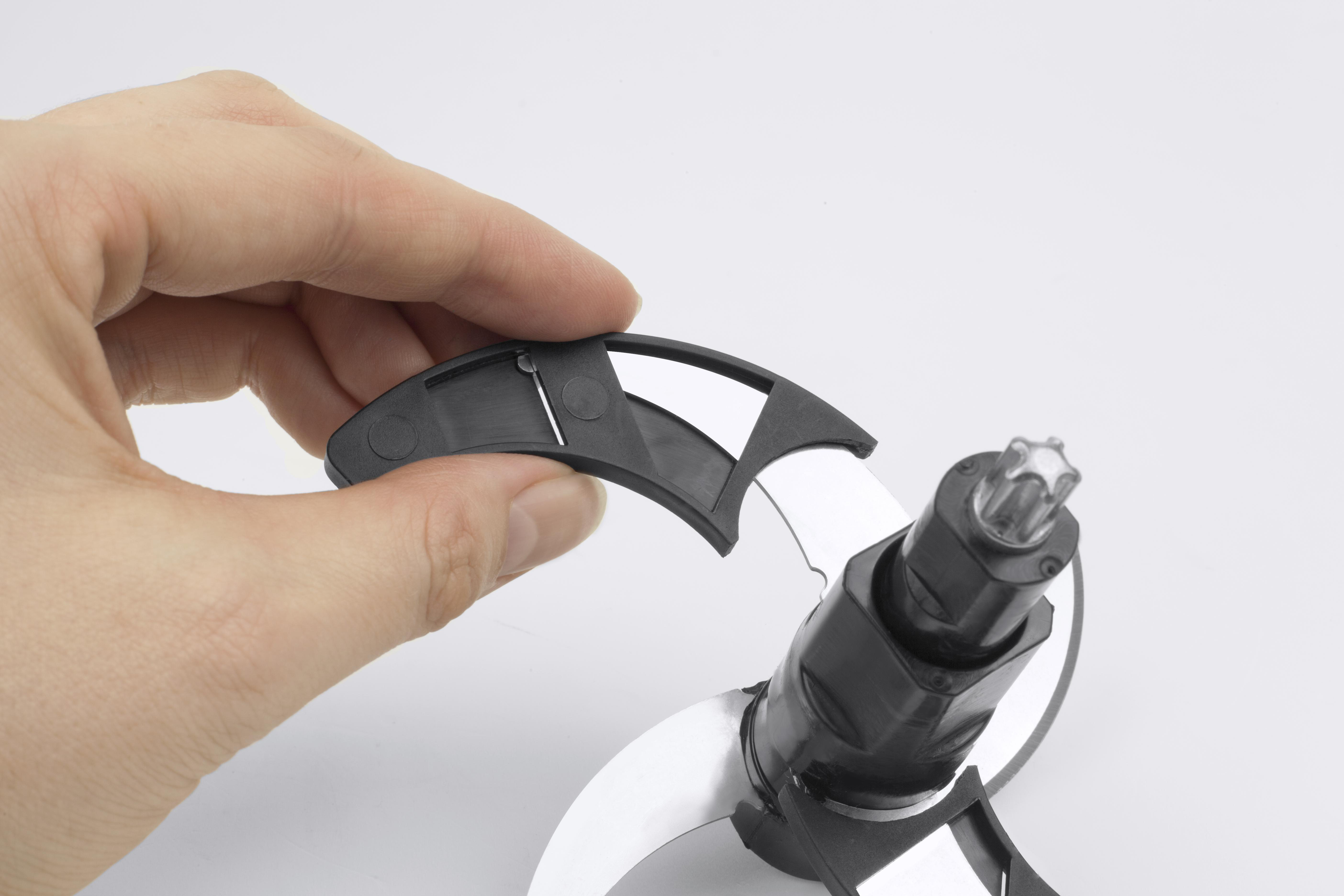 Eine Hand hält ein schwarzes Teil über einem Küchenmaschinenaufsatz mit Klingen.