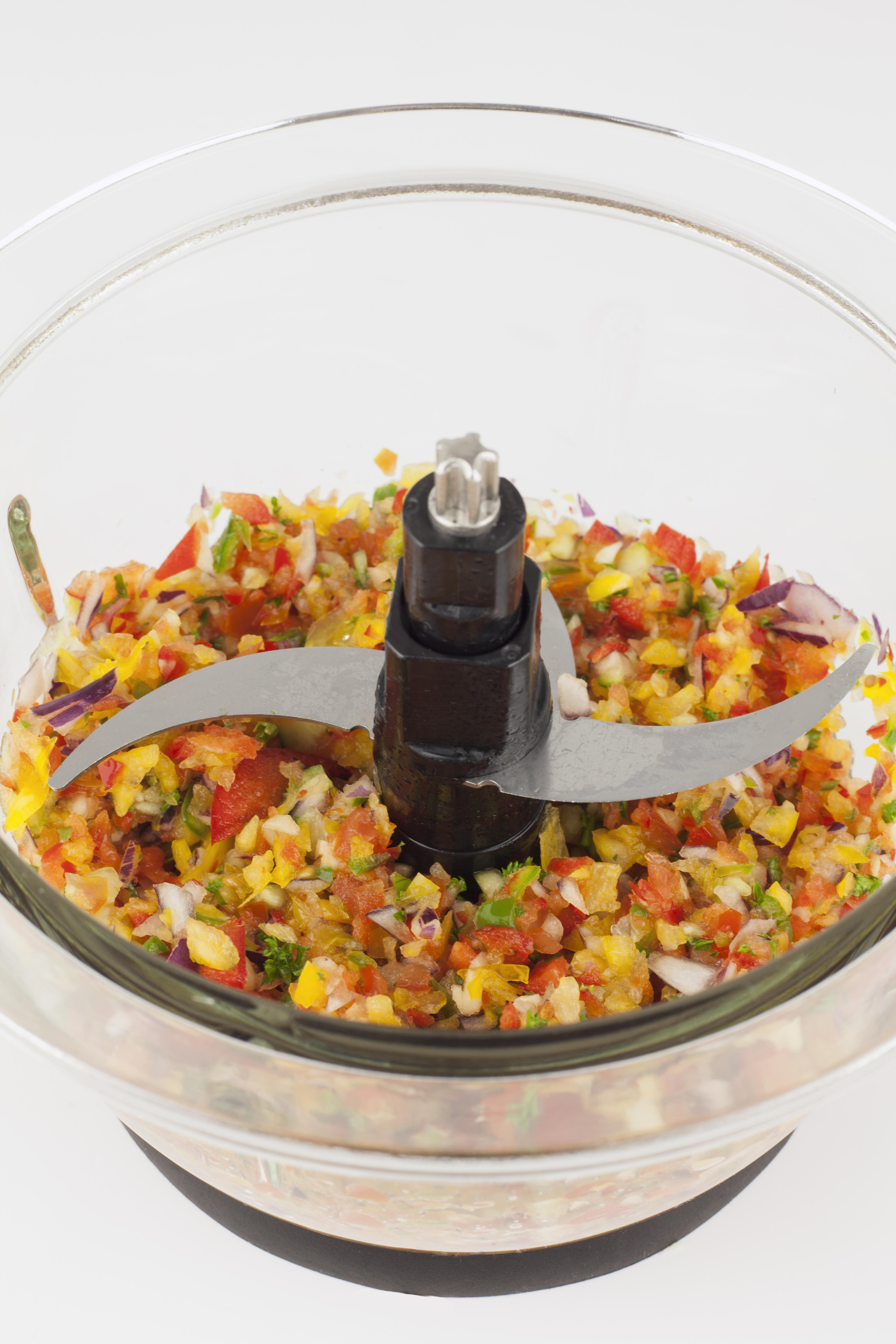 Zerkleinerte Tomaten, Zwiebeln, Paprika und Kräuter in einem Mixer.