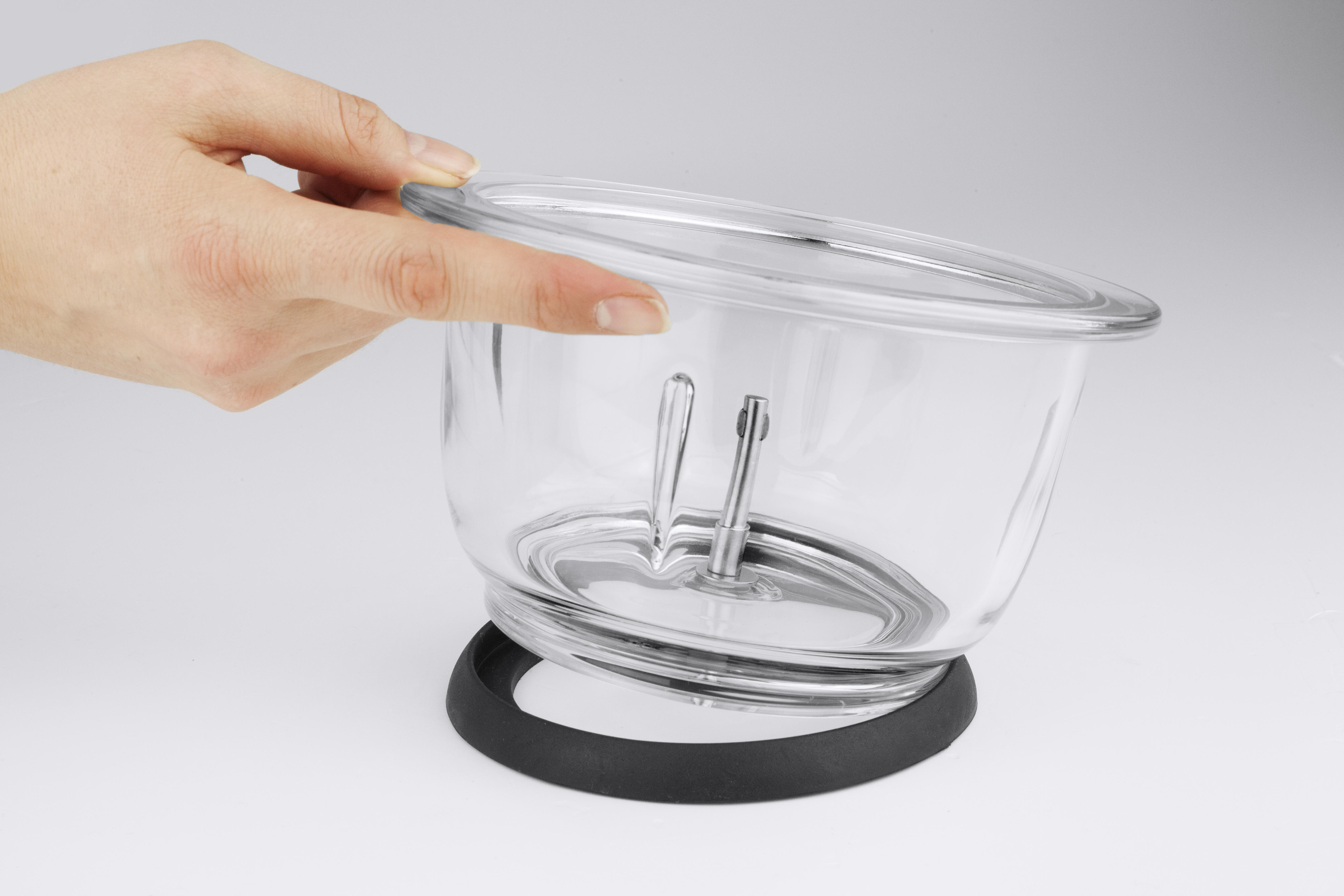 Eine Hand hält einen durchsichtigen Glasbehälter mit Metallstäben und schwarzem Sockel.