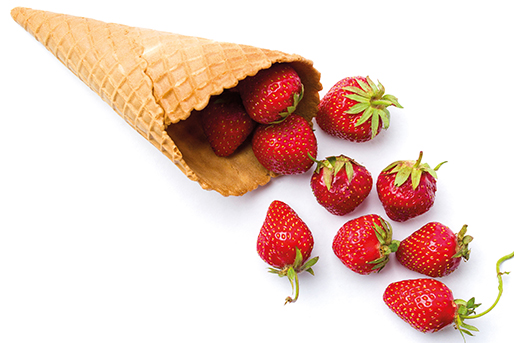 Aardbeien die uit een wafelkegel vallen op een witte achtergrond. Rode bessen met groene stelen.