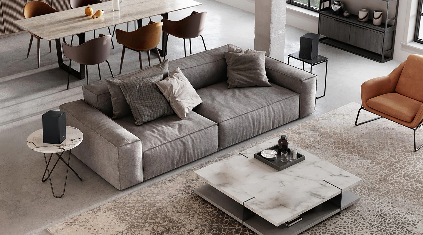 Salon avec canapé gris, table en marbre et enceintes. La scène est bien éclairée et moderne.