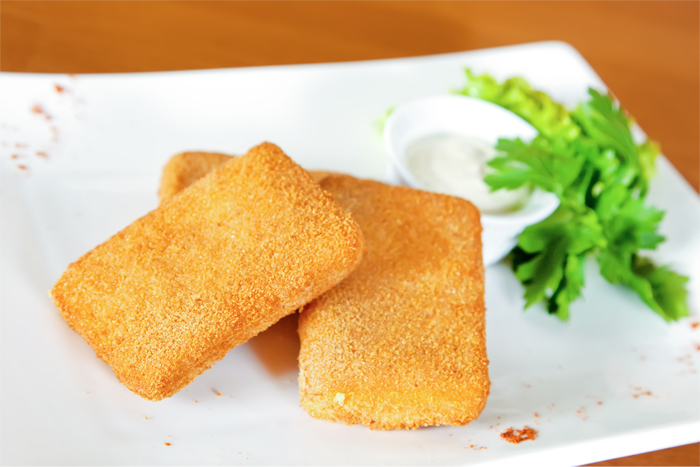 Trois rectangles de fromage panés et frits sur une assiette blanche avec garniture et sauce.