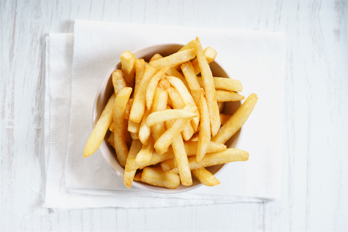Un bol de frites sur une serviette blanche, contre un fond en bois blanc.