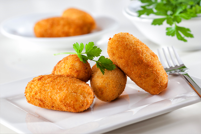 Quatre croquettes dorées sur une assiette blanche avec du persil.
