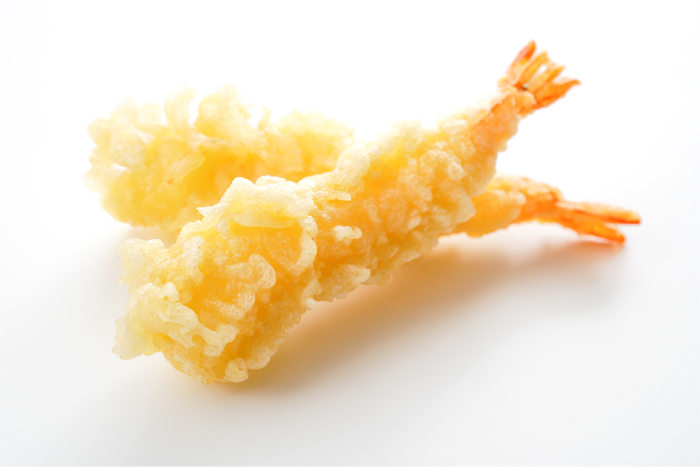 Twee tempura garnalen op wit oppervlak, goudbruin met oranje staarten.