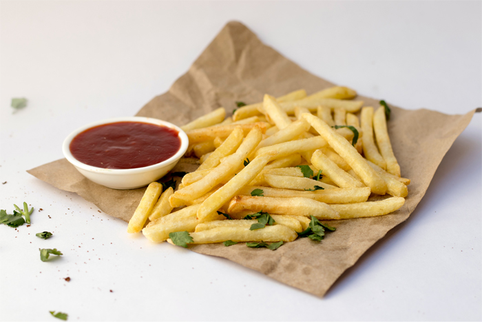 French fries on brown paper with parsley and a bowl of ketchup on a white background.