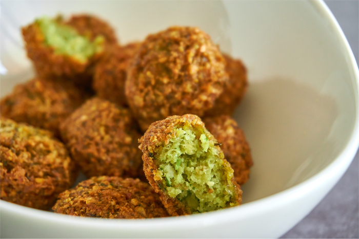 Falafel balls in a white bowl. One is cut in half showing green interior and other balls are visible.